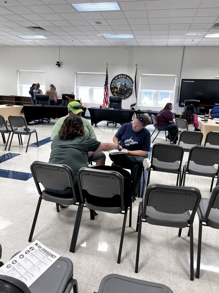 Several staff members sit at tables in a training room, looking toward a person speaking off-camera. Their body language suggests thoughtful discussion as they participate in the exercise.