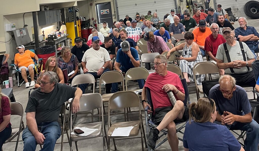 Hampshire County Schools bus drivers and transportation staff gathered for a training session inside the transportation garage. Employees are seated in rows while participating in back-to-school preparation and safety training. The garage setting, equipment, and work areas are visible around the group.
