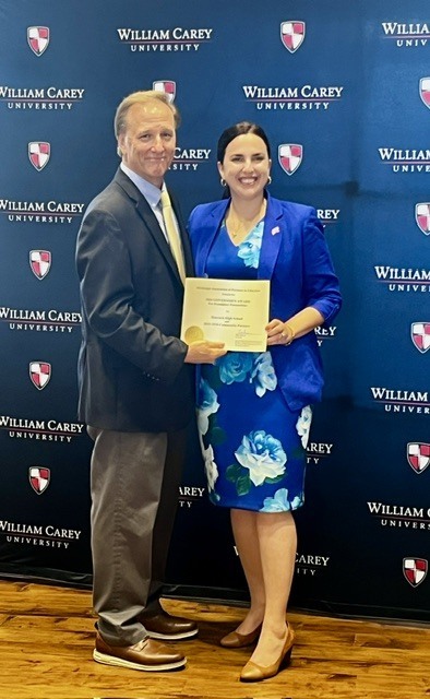 A man with a sport coat and khakis next to a woman in a blue dress with a blue blazer