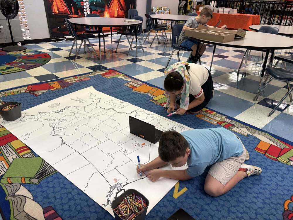 Two students on the floor working on a large map of the United States