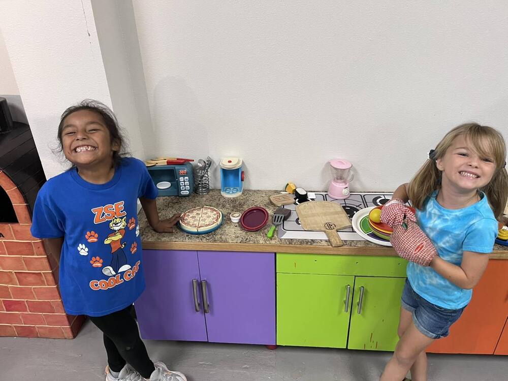 two kindergartners playing at the pretend cooking station