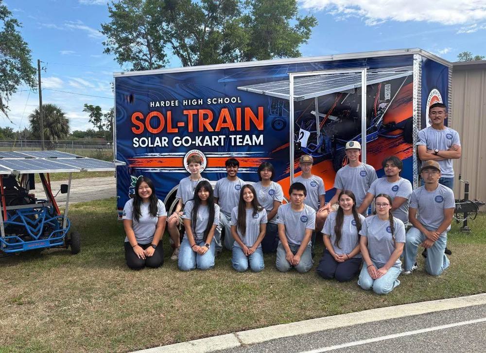 students kneeling in front of a HHS sol-train solar go-kart team trailer