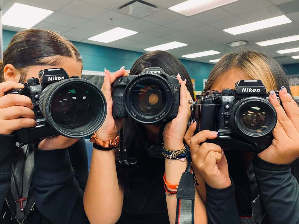 three students pointing cameras