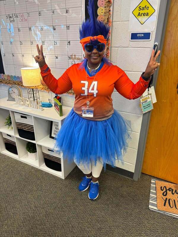staff member dressed up with blue hair, shoes, and tutu, orange jersey, and peace signs