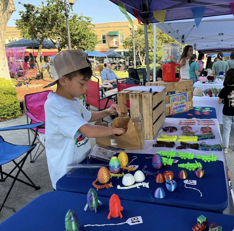 Boy bagging a purchased item  from his table of 3d printed figures