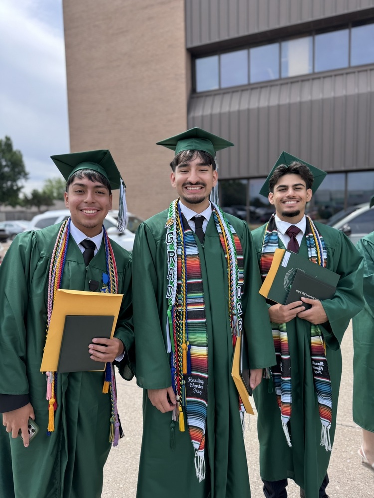 Three male graduates stand outside smiling before the graudation cap toss