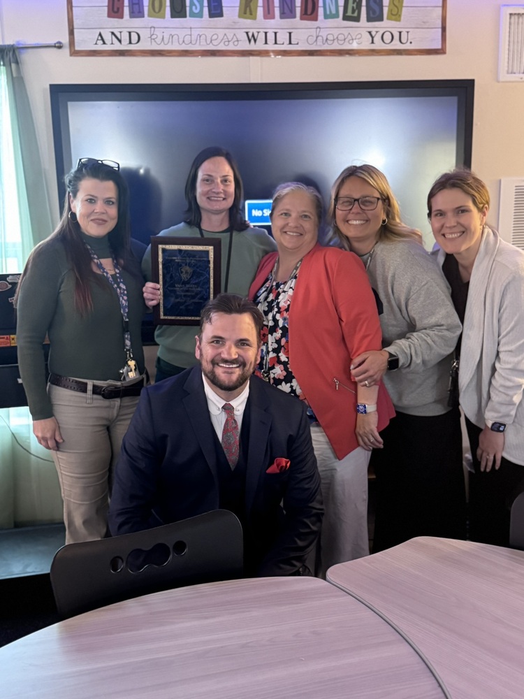 Megan Knudson, HCPMS's teacher of the year, stands with the HCPMS leadership team. She holds her award and smiles.