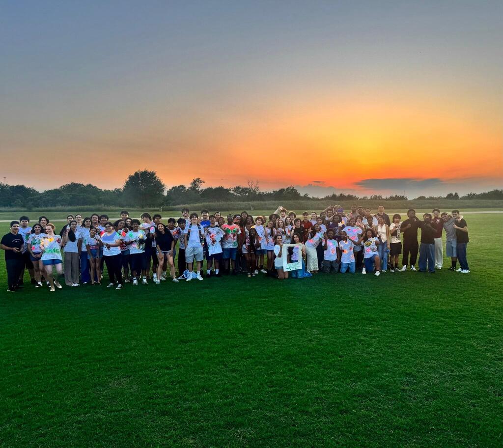HCP Seniors pose for a photo on a grassy field with a sunset in the background.