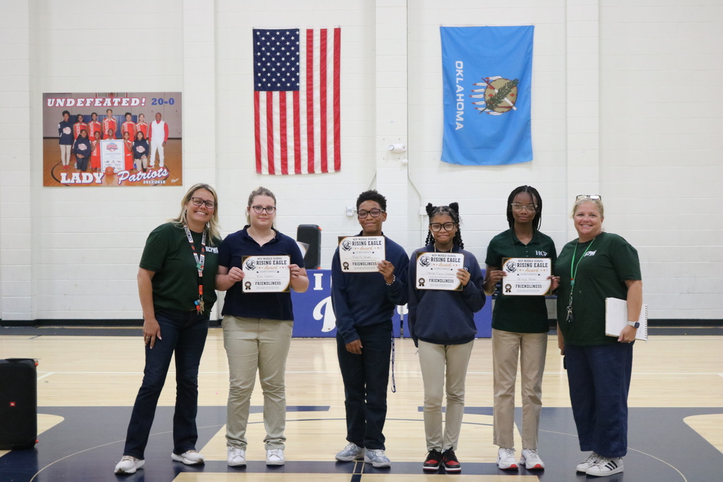 Six individuals stand in a line, holding certificates. They are in a gym with a basketball court.