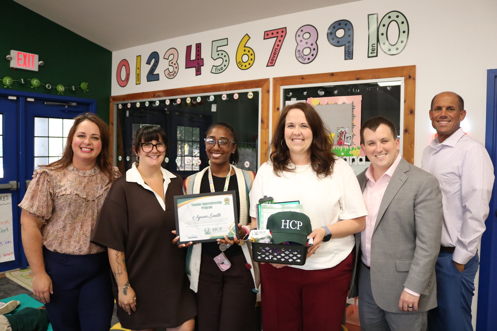 Teacher receiving an Award from District leadership pose with certificate and swag basket.
