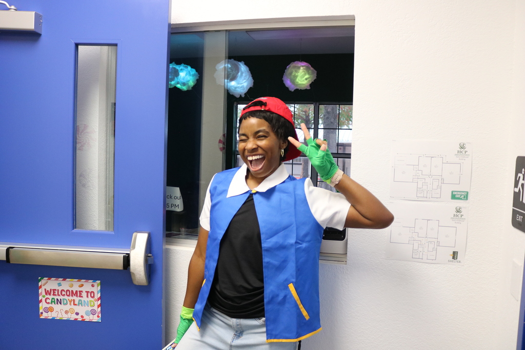Person in blue apron and red hat smiling, standing by blue door. Colorful decor and signs on wall.