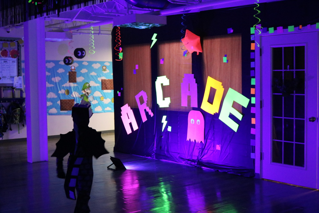 A person in front of a wall that says "Arcade" in multicolored letters. A wall behind has colorful art.