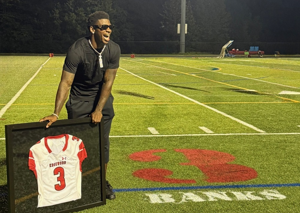 Football player holding his jersey that is number 3 on the side of the football field