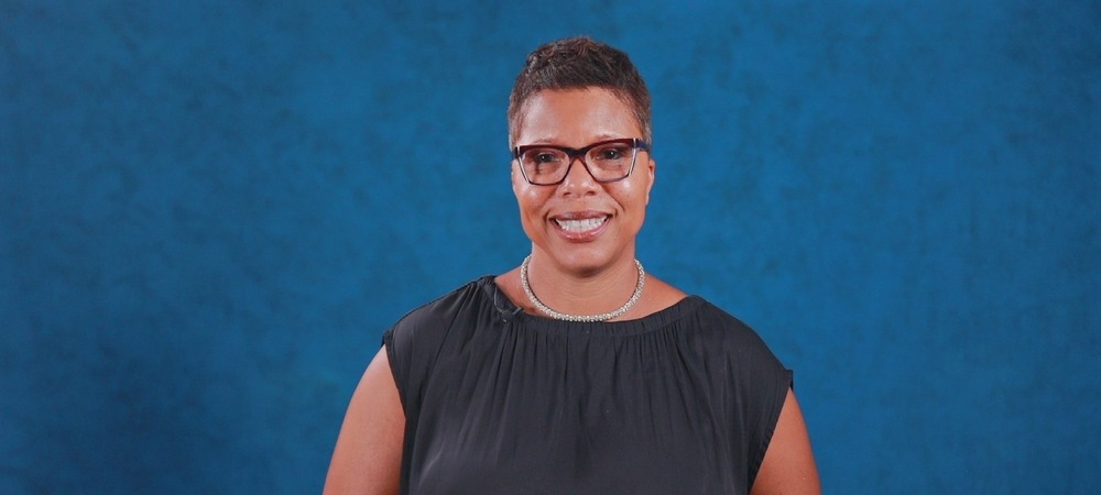 Dr Dyann Mack in front of a blue screen wearing a black blazer