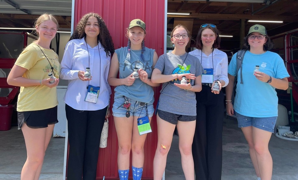 Six Future Farmers of America students from North Harford High School pose and smile in front of a red barn