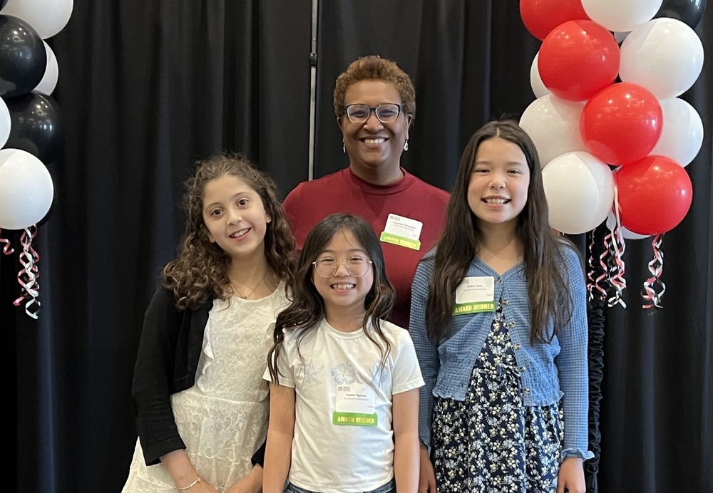 Three students and a teacher pose for a photo on a stage