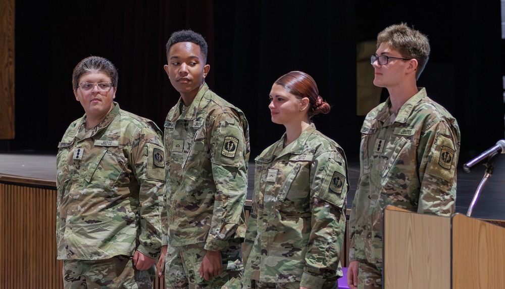 Four students in army uniforms stand in an auditorium