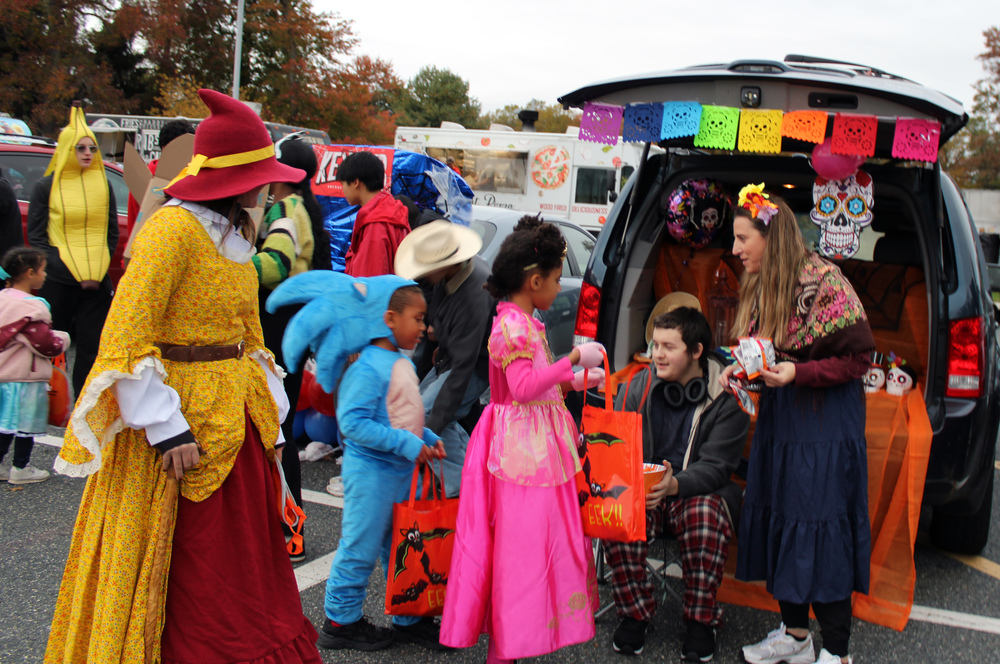 People in colorful costumes trick or treating at a car.