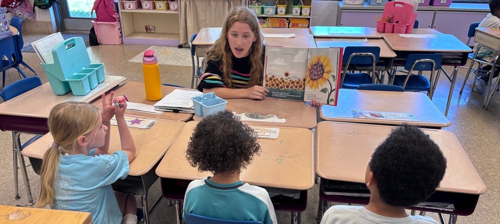 Educator Rising High School student reading a book to three Elementary School students