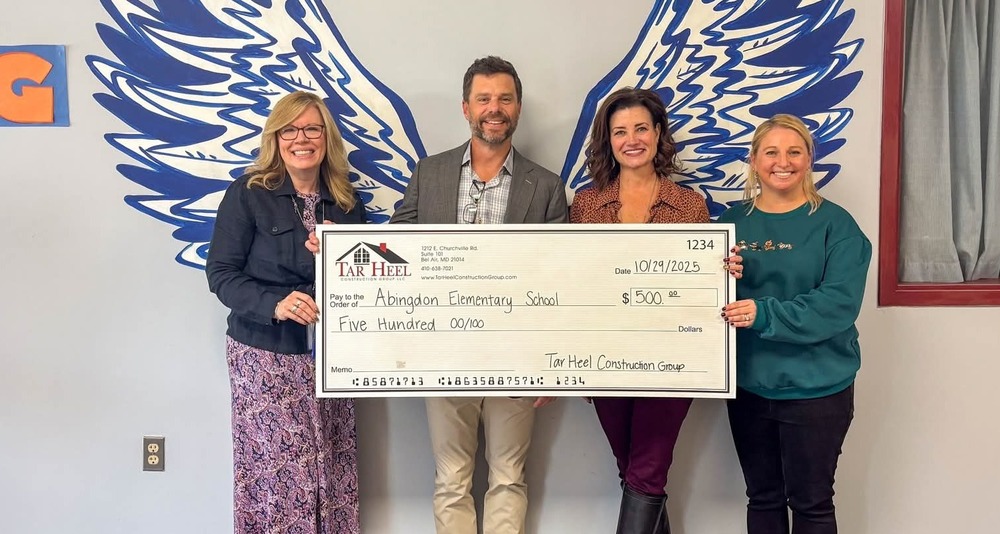 Four people stand holding a fake giant check made out to Abingdon Elementary School