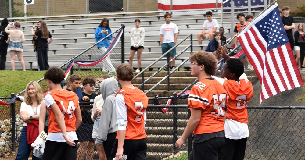 Group of students in orange jerseys walking holding an american flag