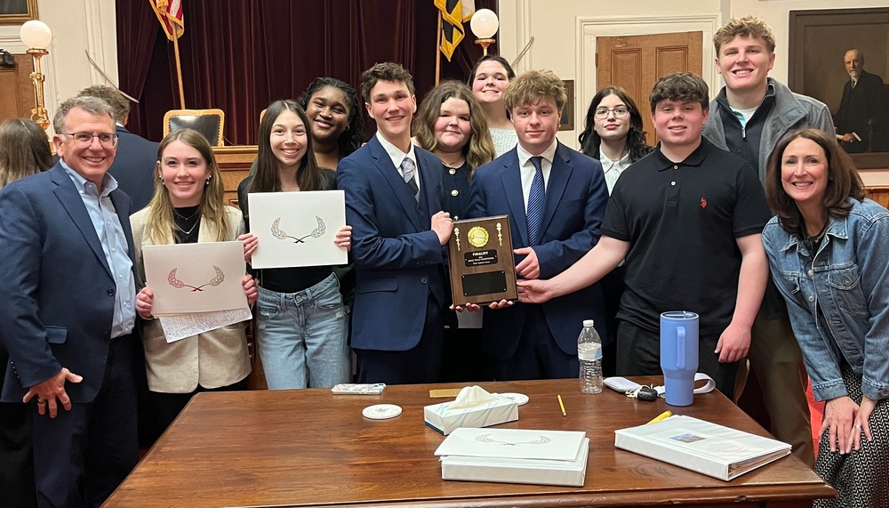 Group of stduents and twon adults standing in a courtroom holding a plaque
