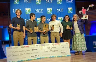 Students from the North Harford High School Envirothon Team pose with their advisor on a stage. Giant checks representing their scholarships are at their feet