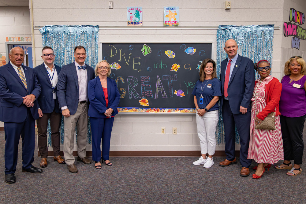 Group of VIPs standing next to a blackboard on the first day of school