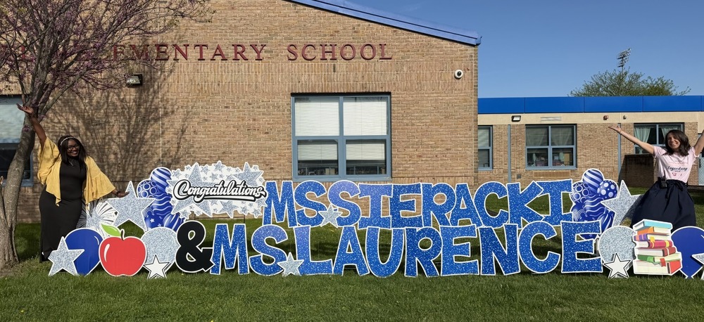 Two women stand in front of Bakerfield Elementary School next to a sign with their names.