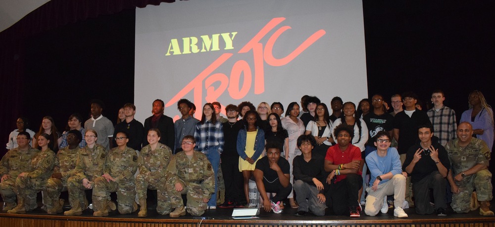 Group of JROTC students on a stage behind them on a big screen are words "Army JROTC"
