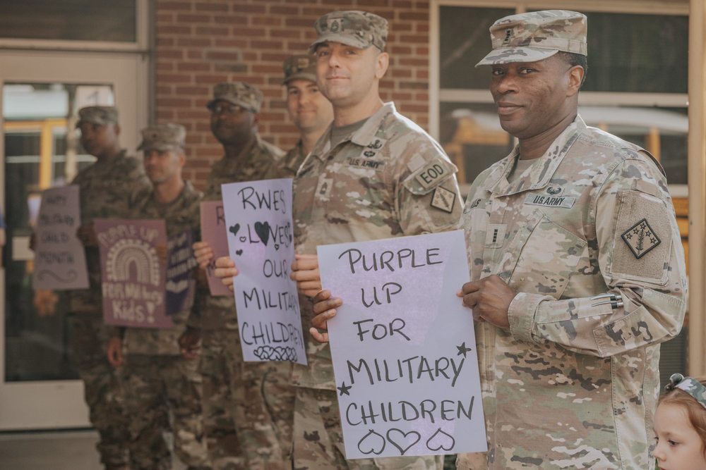 A group of military members stand outside a school holding signs supporting military children and families