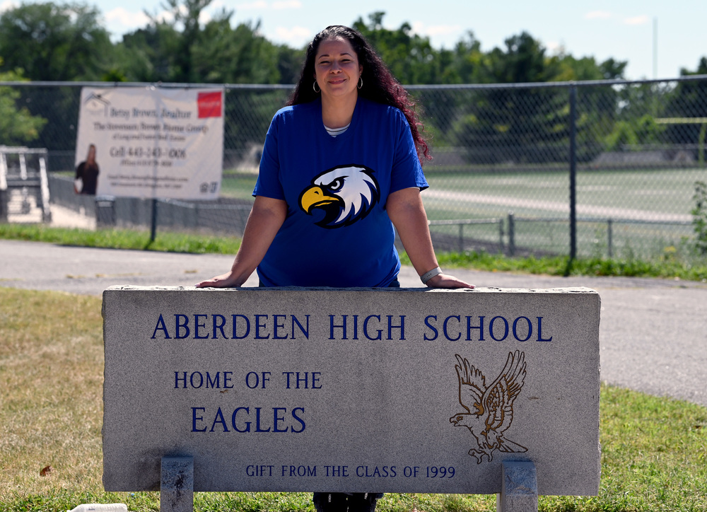 Principal Erica Harris in a blue shirt standing behind a sign that says Aberdeen High School Home of the Eagles