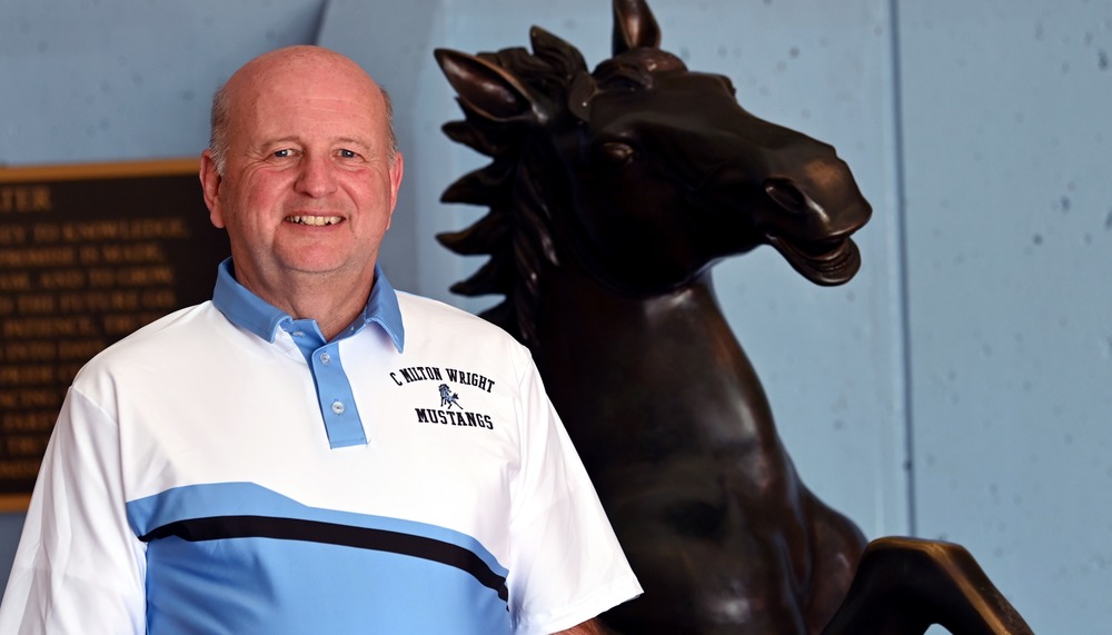 Bryan Pawlicki, new principal of C. Milton Wright High School standing in front of the mustang statue wearing a blue and white C. Milton Wright polo