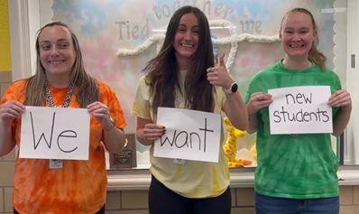 Three teachers at Churchville Elementary School with signs saying we want new students