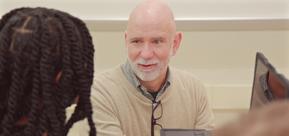 Mr. Michael james in a tan sweater speaking with an african america student