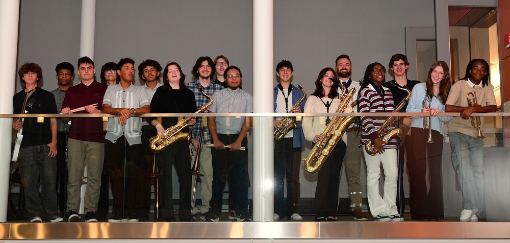 A diverse group of students standing on a balcony holding brass instruments