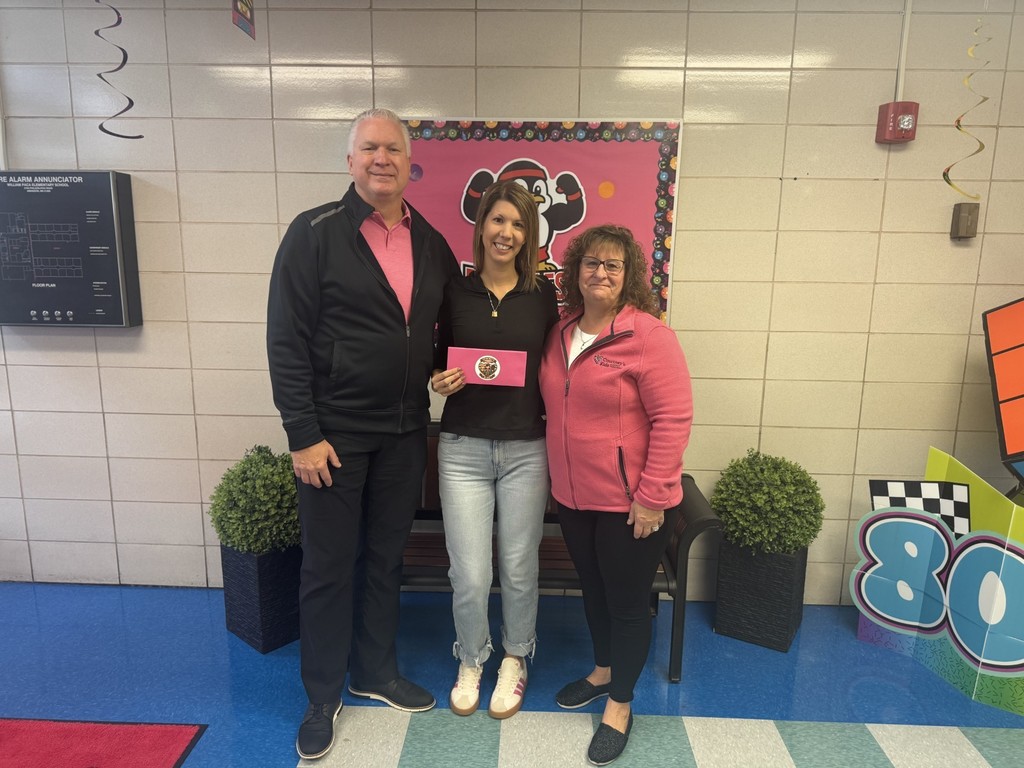 Three people standing and smiling, one in the middle holding a pink envelope