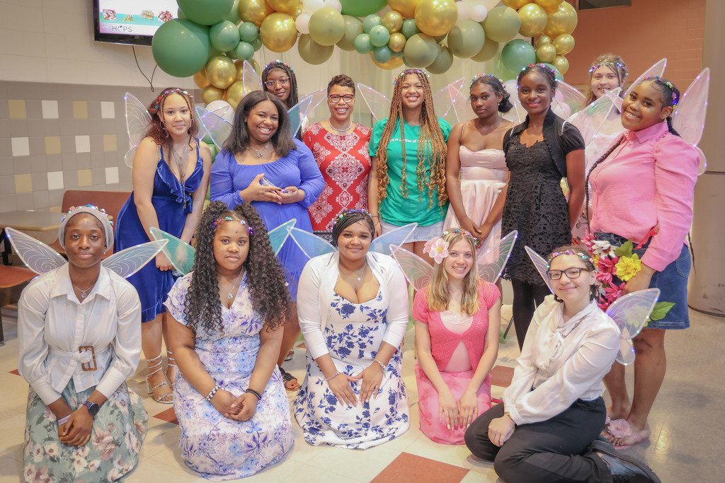 Group of young women wearing fairy wings standing under a balloon arch