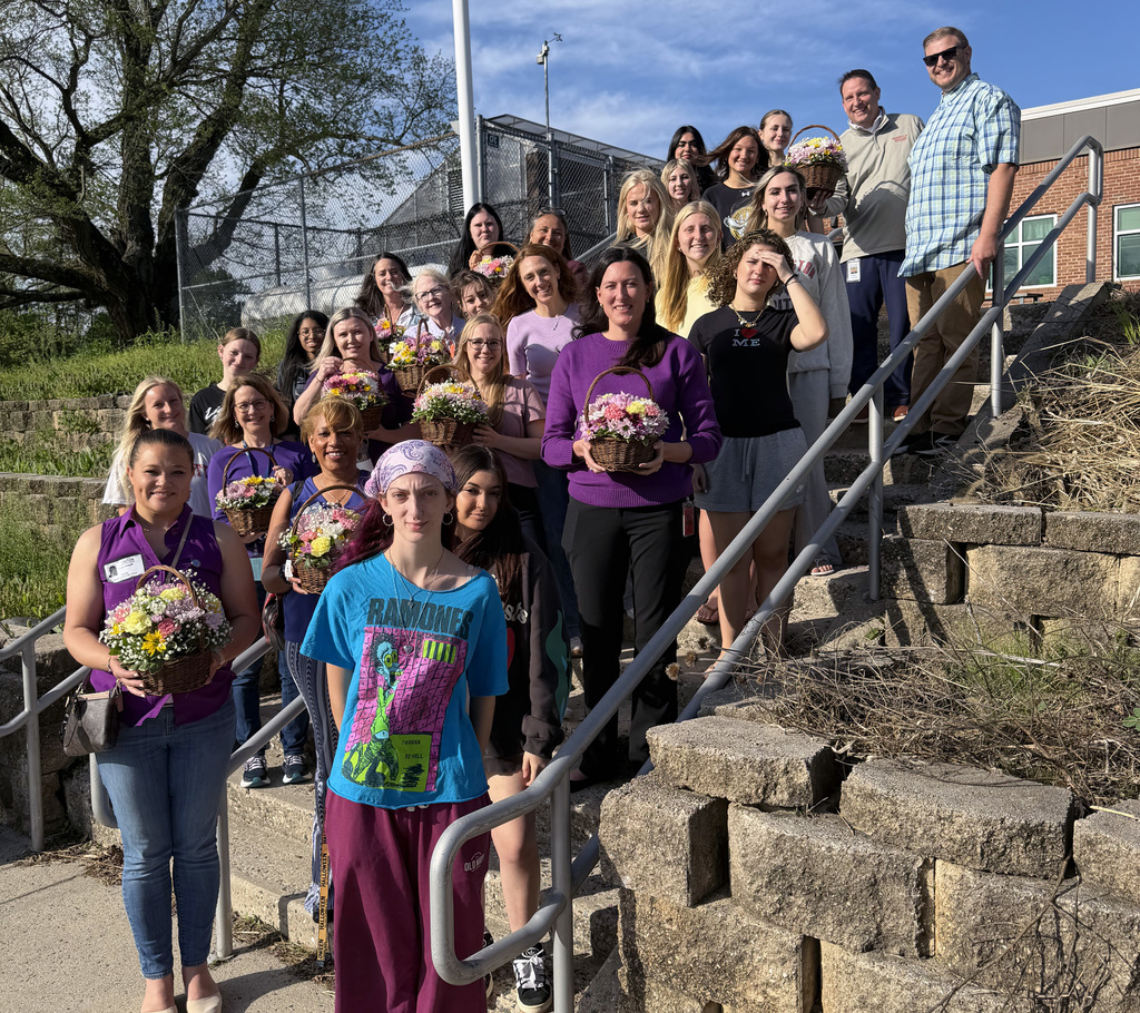 A group of students standing on stairs, many holding plants.