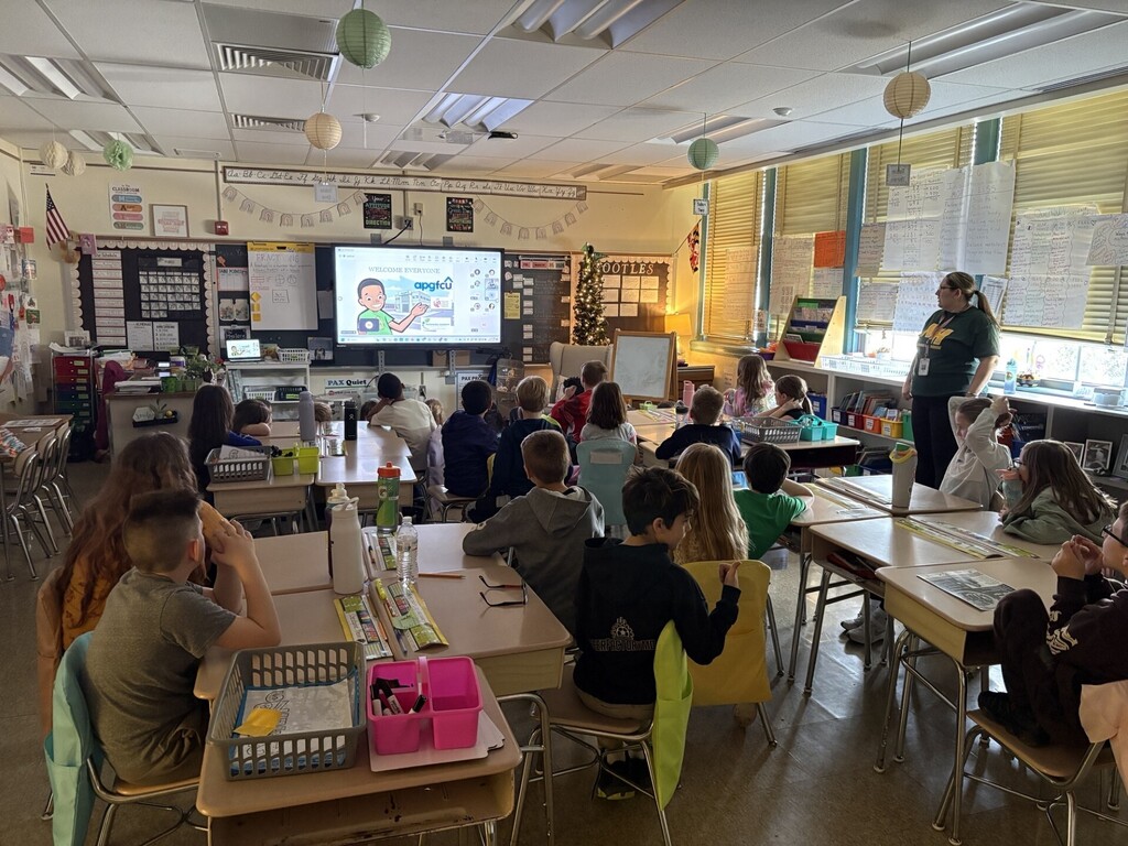 Students in a classroom watching the Danny Dollar Event on a pulldown monitor
