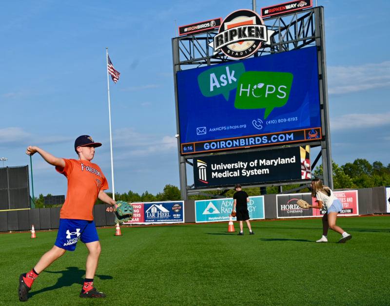 Child wearing an orange shirt throws a baseball on the Ironbirds field