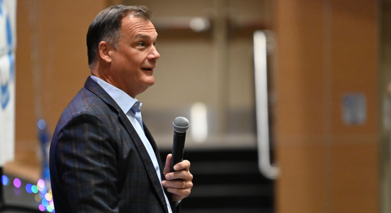 Dr. Sean Bulson, wearing a blue shirt and grey suit jacket speaking into a microphone
