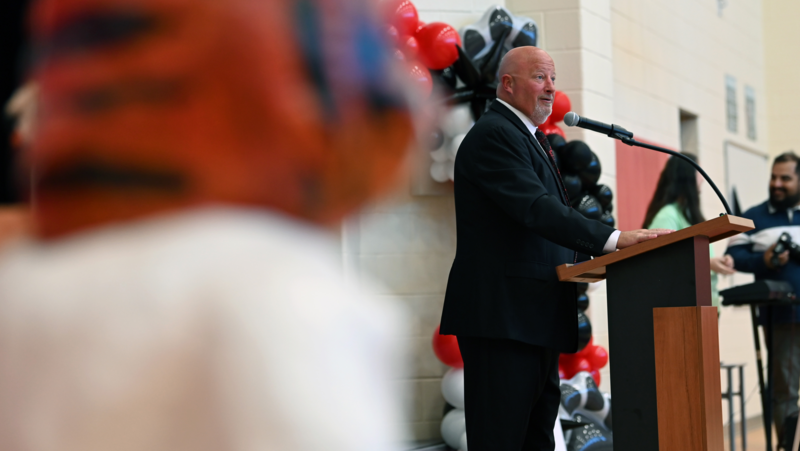 Principal Chris Cook addressing those in attendance, with a tiger statue in the foreground