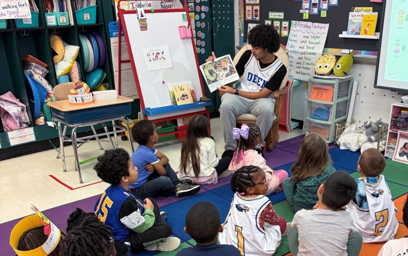 High School student reading a book to Elementary School Students
