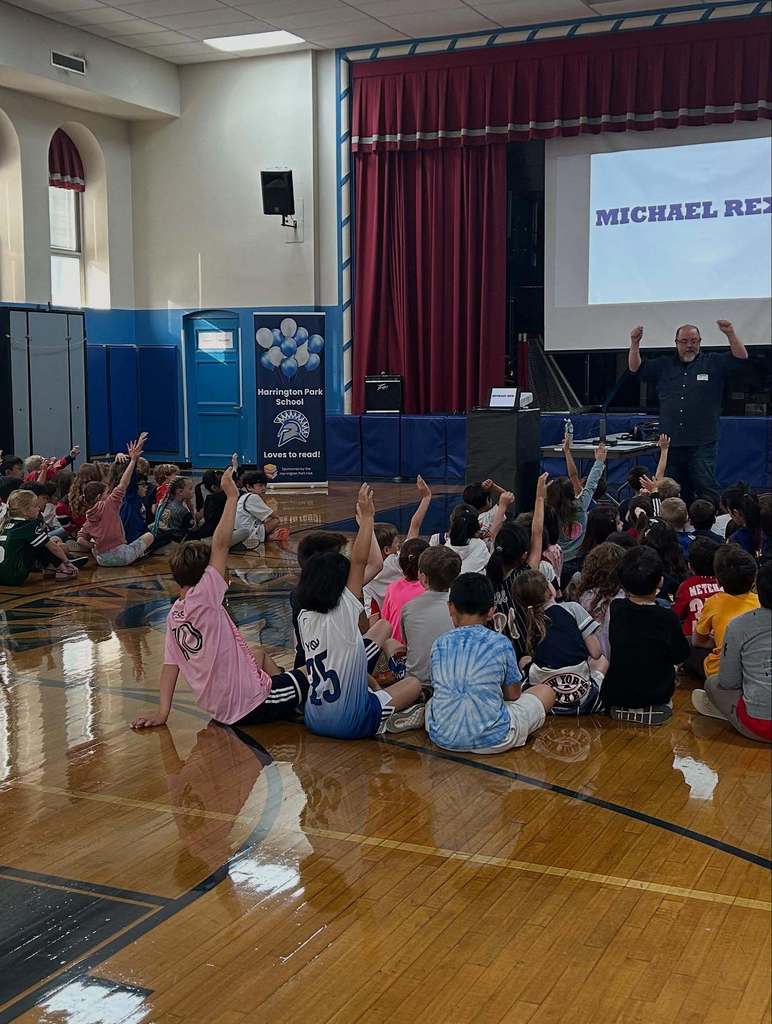 Author Michael Rex engages with students who are raising their hands during an Author Visit at the HP School.