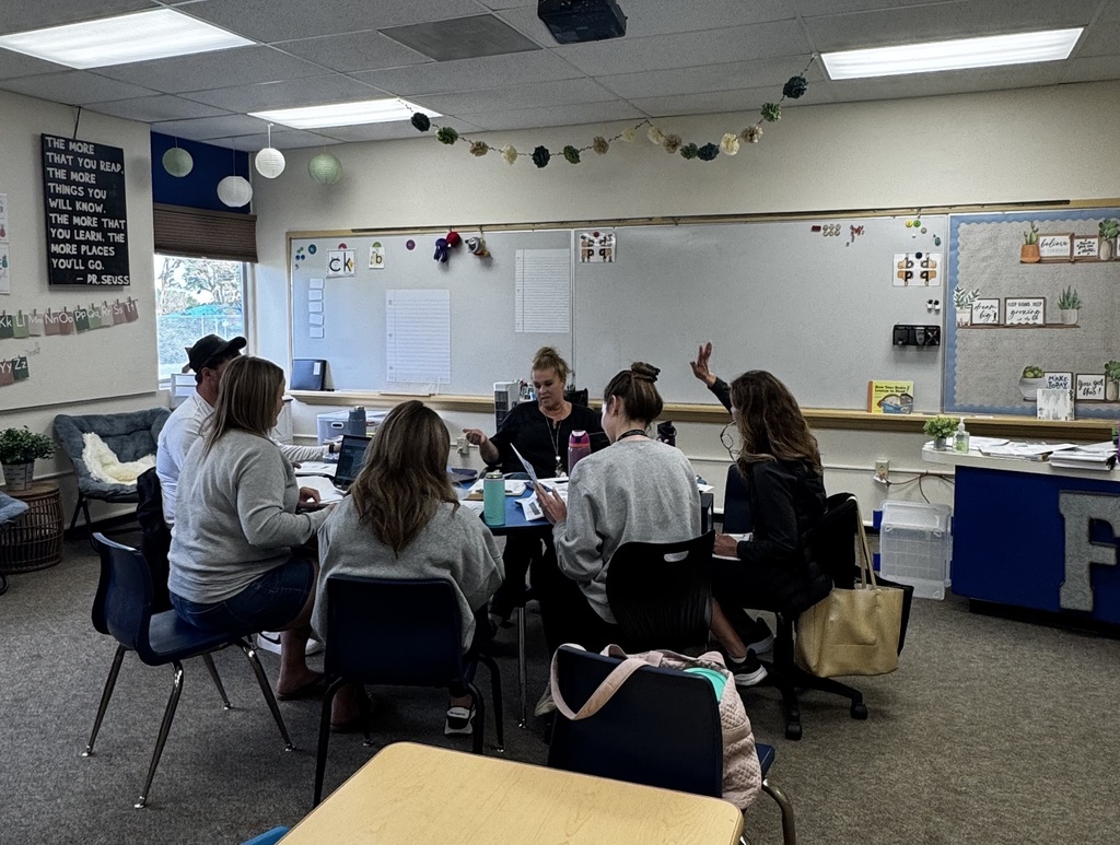 Staff gathered around a semicircle table with some hands raised.