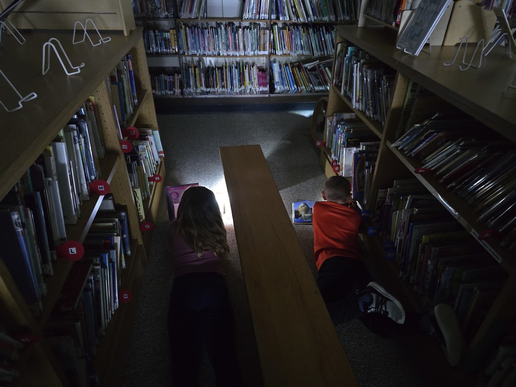 First grade students reading with flashlights in the library