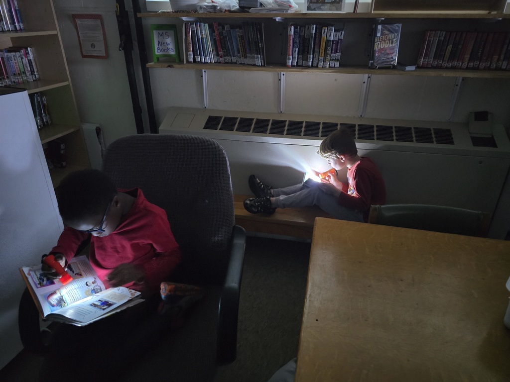 First grade students reading with flashlights in the library