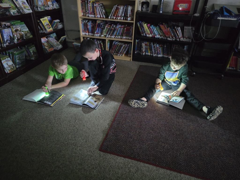 First grade students reading with flashlights in the library