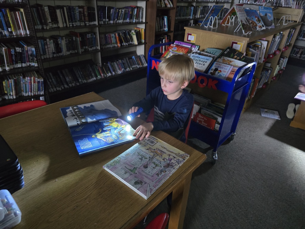 First grade students reading with flashlights in the library
